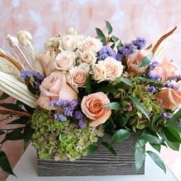 Peach roses and purple filler flowers in a rectangular vase