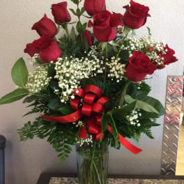 Red roses arranged in a clear glass vase with baby's breath and a red ribbon