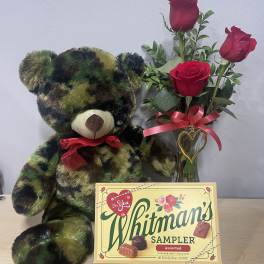 Teddy bear beside red roses in a glass vase and a Whitman's chocolate box