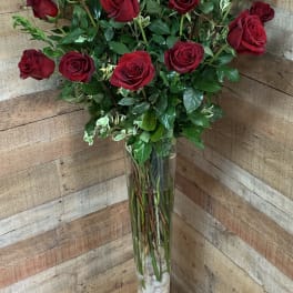 Tall vase arrangement of red roses with greenery