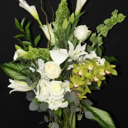 White floral arrangement with orchids, roses, and calla lilies in a glass vase