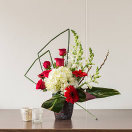 Red roses and gerbera daisies in a dark vase with white hydrangea