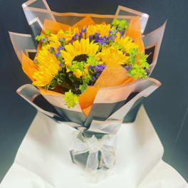 Bouquet of yellow sunflowers with purple filler flowers wrapped in orange and clear paper