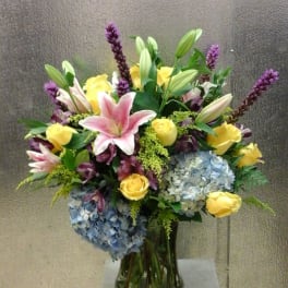 Bouquet of pink lilies, yellow roses, and blue hydrangeas in a glass vase