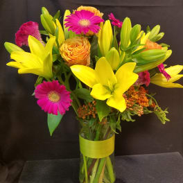 Bouquet of yellow lilies, pink gerbera daisies, and orange roses in a glass vase
