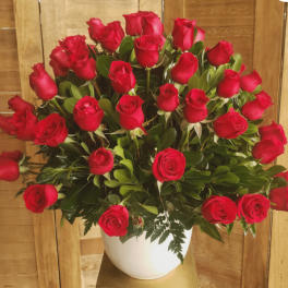 Large arrangement of red roses in a white ceramic pot against a wood background