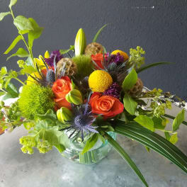 Mixed bouquet with orange roses, yellow blooms, and green accents in a glass vase