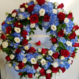 Circular wreath of red roses, blue hydrangeas, and white blooms