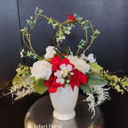 Red and white floral arrangement in a white vase with heart-shaped twig accents