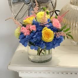 Bouquet of blue hydrangeas, pink roses, and yellow roses in a glass vase