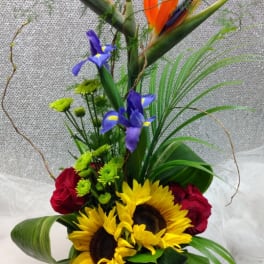 Tropical bouquet with sunflowers, red roses, and bird of paradise in a glass vase