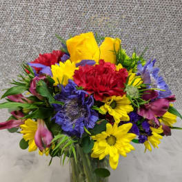 Colorful mixed bouquet in a clear glass vase with yellow, red, purple, and pink blooms