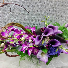 Long modern centerpiece of purple calla lilies and orchids with curved vine accents