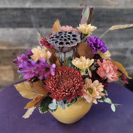 Mixed chrysanthemum arrangement in a yellow vase with dried lotus pod