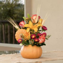 Fall floral arrangement in a pumpkin-shaped container with roses and lilies