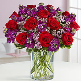 Red roses and purple flowers arranged in a clear glass vase