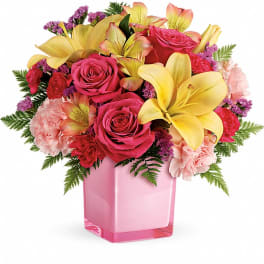 Pink roses and yellow lilies arranged in a pink glass vase