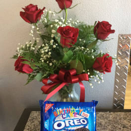 Red roses in a glass vase with a birthday Oreo cookie package in front