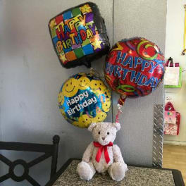 Birthday balloons with a teddy bear sitting below them