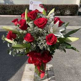 Red roses and white lilies in a glass vase with a red ribbon