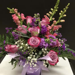 Pink and purple floral arrangement with roses and snapdragons in a ribbon-tied vase