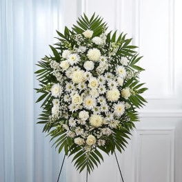 White funeral spray on a stand with palm fronds and mixed blooms