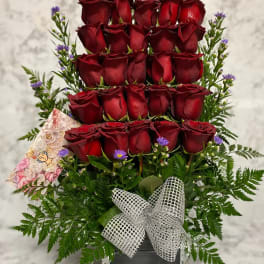 Tall arrangement of tiered red roses with small purple asters in a metal container with a silver bow