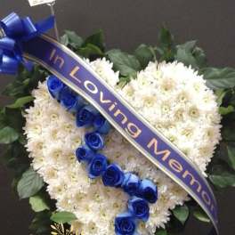 Heart-shaped white flower arrangement with blue roses and a ribbon