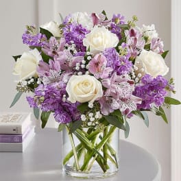 Bouquet of white roses and purple flowers in a clear glass vase