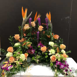 Large floral arrangement with orange roses and purple orchids on a white base