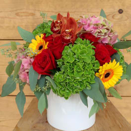 Bouquet of red roses, green hydrangea, and yellow gerbera daisies in a white vase