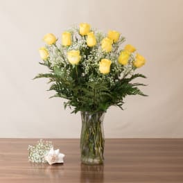 Tall arrangement of yellow roses with white accent flowers in a clear glass vase