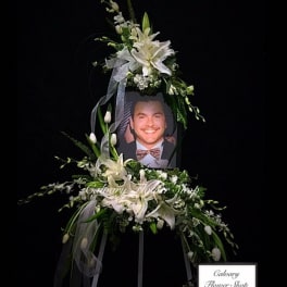White lily funeral spray around a framed portrait on a stand