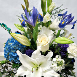 White lilies, blue irises, and a blue hydrangea arrangement in a glass vase