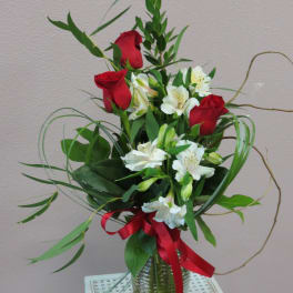 Red roses and white alstroemeria in a glass vase with a red ribbon
