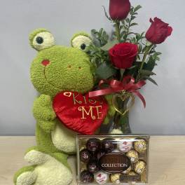 Stuffed frog holding a heart beside red roses and a box of chocolates