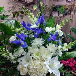 Tall arrangement of blue irises and white lilies, hydrangeas, and mums in a woven basket