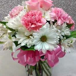 Pink roses and carnations with white daisies in a glass vase with a pink ribbon bow
