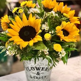 Bouquet of yellow sunflowers and small white flowers in a metal container
