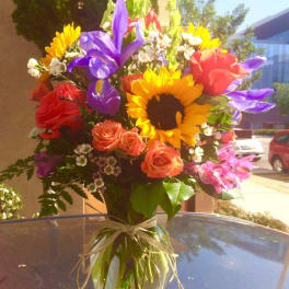 Colorful bouquet of sunflowers, roses, and purple flowers in a glass vase