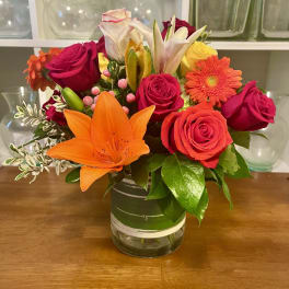 Mixed bouquet of roses, lilies, and a gerbera daisy in a glass vase
