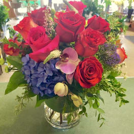 Red roses with blue hydrangea and orchids in a glass vase