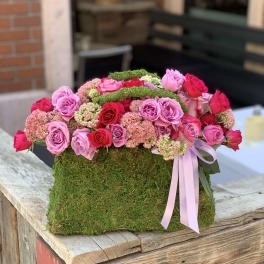 Pink and red roses arranged in a moss-covered box with a ribbon