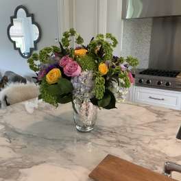 Mixed bouquet of pink, yellow, and lavender flowers in a glass vase