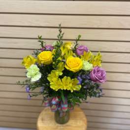 Bouquet of yellow and lavender flowers in a glass vase with a ribbon