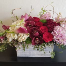 Arrangement of red roses, orchids, calla lilies, and pink hydrangeas in a white box