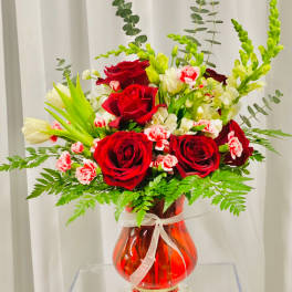 Red roses and pink carnations in a red glass vase with a white ribbon