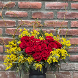 Red roses arranged with yellow filler flowers in a black vase