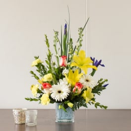 Mixed bouquet in a square glass vase with yellow lilies, white daisies, and roses