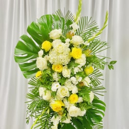 Tall floral standing spray with white and yellow roses and tropical leaves